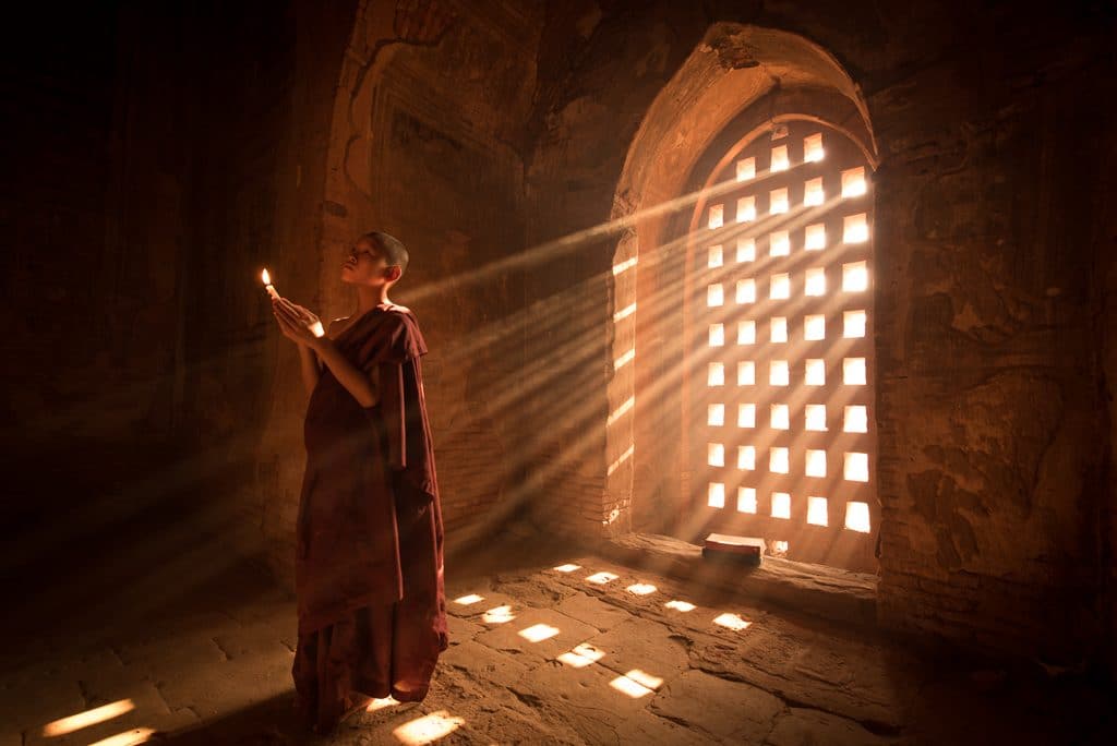 Buddhist monk praying in light rays